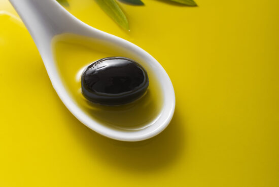 Olive fruit in spoon with oil background close up